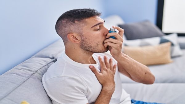 Young hispanic man using inhaler sitting on sofa at home Young hispanic man using inhaler sitting on sofa at home